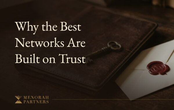 A brass key resting on a closed leather portfolio beside a wax-sealed envelope on a dark wooden desk, with the title “Why the Best Networks Are Built on Trust” and the Menorah Partners logo